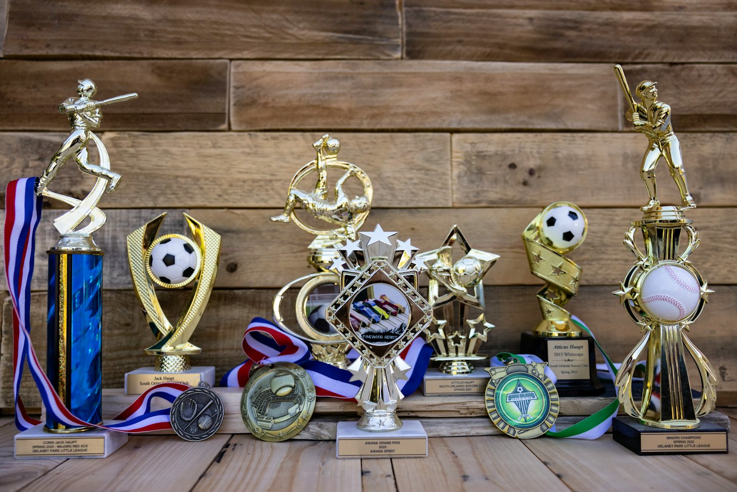 Statuetki sportowe i medale wyeksponowane na rustykalnym drewnianym stole.